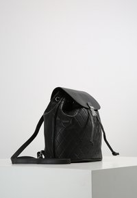 Sac seau en cuir noir matelassé avec fermeture à cordon, poignée latérale et sangle réglable, avec une finition lisse et brillante.