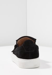 Baskets en daim noir avec une semelle en caoutchouc blanche, présentant une couture le long de la semelle et une doublure intérieure douce. Vue arrière mettant en évidence les détails du design.