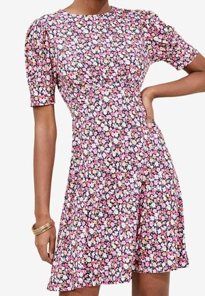 Kurzärmliges Kleid mit rosa, weißem und orangefarbenem Blumenmuster, tailliertem Schnitt und leicht gepufften Schultern, getragen mit goldenen Armreifen am Handgelenk.