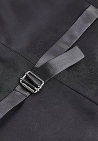 Tejido negro con una textura suave presenta una hebilla de metal plateado y una tira de satén superpuesta para el cierre.