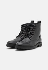 Paire de bottines noires en cuir à lacets, avec semelles robustes et languettes de traction, présentées sur un fond blanc.
