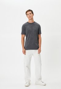 Mørkegrå t-shirt med korte ærmer og rund halsudskæring, sammen med hvide cargo-bukser med sidelommer og hvide sneakers.