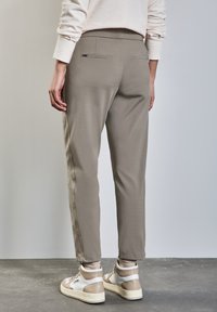 Ljusgrå byxor i slätt tyg, med slim fit, bakfickor och elastisk midja, som bärs med beige och vita sneakers.