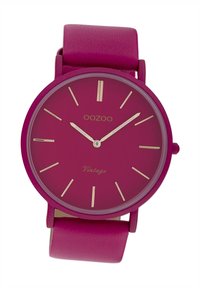 Montre ronde avec un bracelet en cuir fuchsia et un cadran fuchsia assorti. Index et aiguilles dorés. "Oozoo Vintage" imprimé sur le cadran.