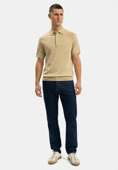 Beige polo skjorta med ribbad krage och tre knappar, bärs med mörkblå jeans och krämfärgade sneakers med en ljusbrun sula.