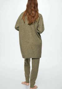 Olivově zelený pletený svetr a odpovídající kalhoty z měkké látky. Svetr je oversized s kulatým lemem a kalhoty jsou slim fit.