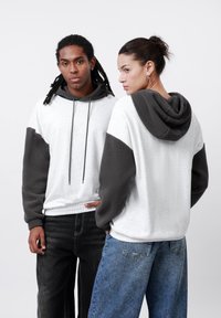 Sudadera con capucha de color gris claro en el cuerpo y mangas de forro polar gris oscuro. Presenta un cordón, un ajuste relajado y dos personas que la llevan puesta.