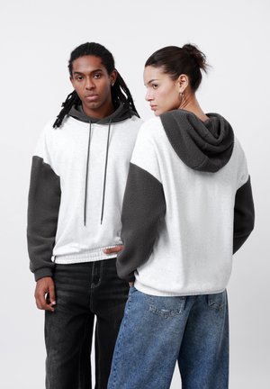 Hooded sweatshirt with a light gray body and dark gray fleece sleeves. Features a drawstring, relaxed fit, and two individuals wearing it.