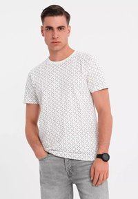 Bílý tričko s krátkým rukávem s geometrickým černým vzorem, kulatým výstřihem a bavlněným materiálem; spárováno se světlými šedými džíny.