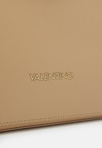 Tan leather product featuring embossed "VALENTINO" logo in gold. Smooth texture with subtle stitching detail, rectangular shape.