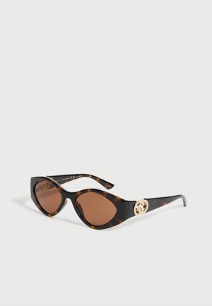 Zonnebril met schildpadmotief in kattenoogvorm, bruine getinte lenzen en een gouden Gucci-logo op de pootjes.