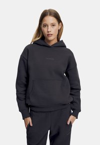 Mørk grå hettegenser laget av myk stoff, med kengurulomme, ribbestrikkede mansjetter, og en minimalistisk logo på brystet.