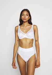 Weißer BH aus transparentem Mesh mit floralem Muster, kombiniert mit hochgeschnittenen weißen Briefs. Sanfte Textur, minimalistisches Design, keine sichtbaren Beschläge.
