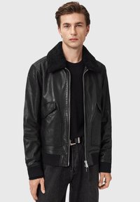 Sort læderbomberjakke med en blød krave, lynlåslukning foran og to lommer. Stylet med en tætsiddende sort sweater og mørke jeans.