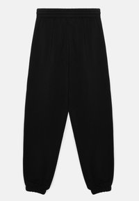 Černé tepláky vyrobené z měkké látky, s elastickým pasem, vypasovanými nohavicemi a staženými manžetami u kotníků.