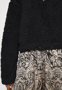 Zwarte fleece trui van getextureerde, pluizige stof. Combinatie met broek met een patroon dat een ingewikkeld paisleydesign in beige, blauw en zwart toont.