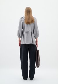 Hallukas hall peplum-särgid koos puffse varrukatega, millele on lisatud lõdvad mustad püksid. Model hoiab ühes käes pruuni nahksegu.