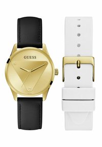 Montre ronde dorée avec un cadran en forme de triangle, bracelet en cuir noir et option de bracelet en silicone blanc. Présente un design minimaliste avec des accents dorés.