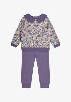 Balta megztinis su gėlių raštu, purpurinė apykaklė su įsiuvais, ir purpurinės šonkaidės kelnės su sagomis ant apačios.