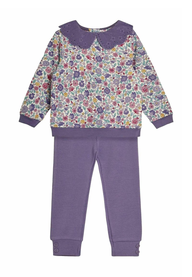 Blomstermønstrede pullover i hvid, lilla krave med bølgende kanter, og lilla ribbede bukser med knaplukninger.