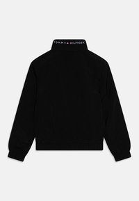 Zwarte jas met elastische manchetten en tailleband, met een hoge kraag. Op de achterkant staat het "TOMMY HILFIGER" logo in wit en rood.