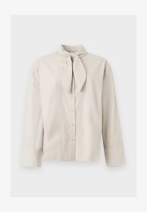 Beige langermet bluse med knapper, bundet nakkedetalj og brede mansjetter på ermene, vist på en ensfarget lys bakgrunn.