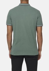 Groene polo met een tweekleurige kraag, voorzien van witte en zwarte strepen. Korte mouwen met bijpassende manchetten, gemaakt van zachte katoen.