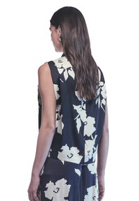 Top senza maniche di colore blu navy con motivo floreale bianco, caratterizzato da una vestibilità rilassata e un tessuto morbido. La vista posteriore mostra un scollo basso e un design delle spalle.