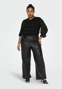 Blusa nera con strisce testurizzate e maniche ¾, abbinata a pantaloni neri a gamba larga in ecopelle a vita alta. Decolleté neri aperti.
