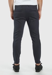 Pantalons slim-fit navy en tissu texturé, dotés de poches arrière avec des détails discrets et des coutures visibles. Bas de jambe lisse.