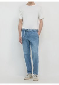 T-shirt blanc léger à manches courtes associé à un pantalon en denim bleu clair avec une ceinture à motif réglable et des poches latérales.