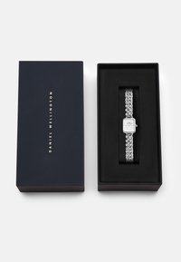 Silberne Armbanduhr mit rechteckigem weißen Zifferblatt und Gliederarmband, präsentiert in einer dunkelblauen Box mit goldener Schrift.