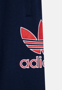 Peça de vestuário azul marinho com logótipo bordado da adidas em vermelho e branco e design trefoil. Textura suave, estilo de vestuário desportivo casual.
