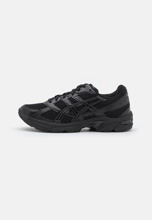 Czarny sportowy sneaker z siateczkową i syntetyczną cholewką, zawiązywany na sznurówki, z teksturowaną podeszwą, pokazany z boku na jednolitym tle.