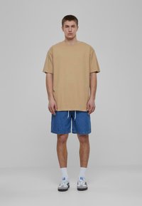 Bežinė per didelė marškinėliai su trumpomis rankovėmis, derinami su mėlynomis džinsinėmis šortais. Balti kojinės ir juodi/balti sportbačiai užbaigia aprangą.