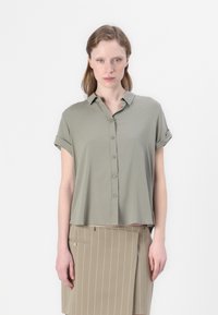 Light olive green short-sleeve shirt with a collar, featuring a button-down front and rolled cuffs, paired with a beige pinstriped skirt.