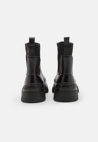 Bottines noires avec une finition brillante, dotées de panneaux élastiques sur les côtés, de languettes de tirage et d'une semelle texturée avec un logo en relief le long du talon.