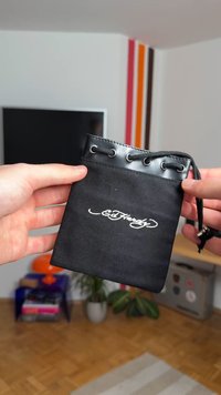 Černý látkový vak s lesklým horním okrajem, kovovými průchodkami a stahovací šňůrkou. Na přední straně je bílé logo.