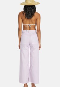 Lichtpaarse wijde broek met hoge taille, twee achterzakken en onafgewerkte zoomdetails, gecombineerd met een eenvoudige haltertop met strik achter.