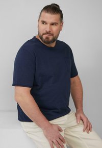 Navyblauwe T-shirt met korte mouwen, gemaakt van zachte katoen, met een klein voorkantzakje. Draagt met lichtbeige broek, met een ontspannen pasvorm.