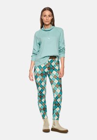 Mint green long-sleeve top with a high collar; patterned leggings in turquoise, brown, and cream diamond shapes; tan ankle boots.
