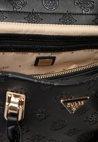 Interno di una borsa nera con loghi in rilievo, fodera beige, chiusura con zip, dettagli metallici e una placca del marchio in tono oro.