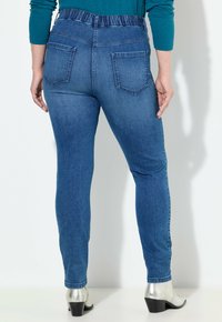 Modré džíny s elastickým páskem, zadními kapsami a slim fit střihem. V páru s metalickými botami na podpatku.