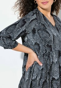 Robe noire avec imprimé serpent gris ; encolure en V, manches trois-quarts, taille froncée et tissu texturé avec des accents brillants.