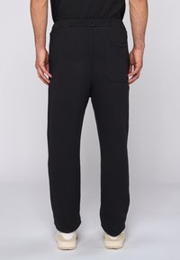 Czarne dresy wykonane z miękkiego materiału, posiadające prosty krój nogawki, elastyczny pas i jedną tylną kieszeń w kwadratowym kształcie.