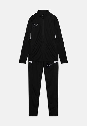 Chándal Nike que presenta una chaqueta negra con cremallera y acentos blancos, junto con pantalones negros a juego, ambos fabricados con tela ligera y suave.