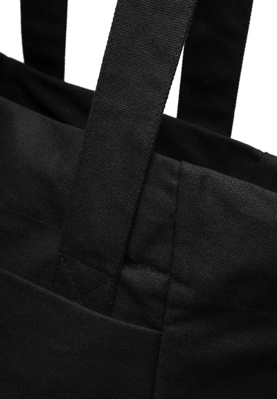 Fekete vászontáska tartós anyagból, két széles fogantyúval és kiemelkedő varrási részletekkel. A textúrája durva és tartós.