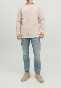 Vaaleanpunainen nappipaita, jossa on puiset napit, yhdistettynä vaaleansinisiin kulutettuihin farkkuihin ja beigheihin kenkiin. Yksinkertainen, rento muotoilu ja malli.