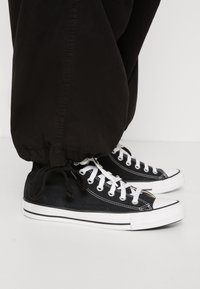 Černé plátěné tenisky s bílými gumovými podrážkami a špičkami. Mají bílé očky a tkaničky, kombinované s černými nohavicemi s manžetami.