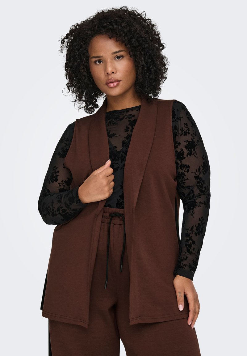 Brown, sleeveless vest in a soft material, layered over a black floral-print long-sleeve top; features a relaxed fit and open front design.